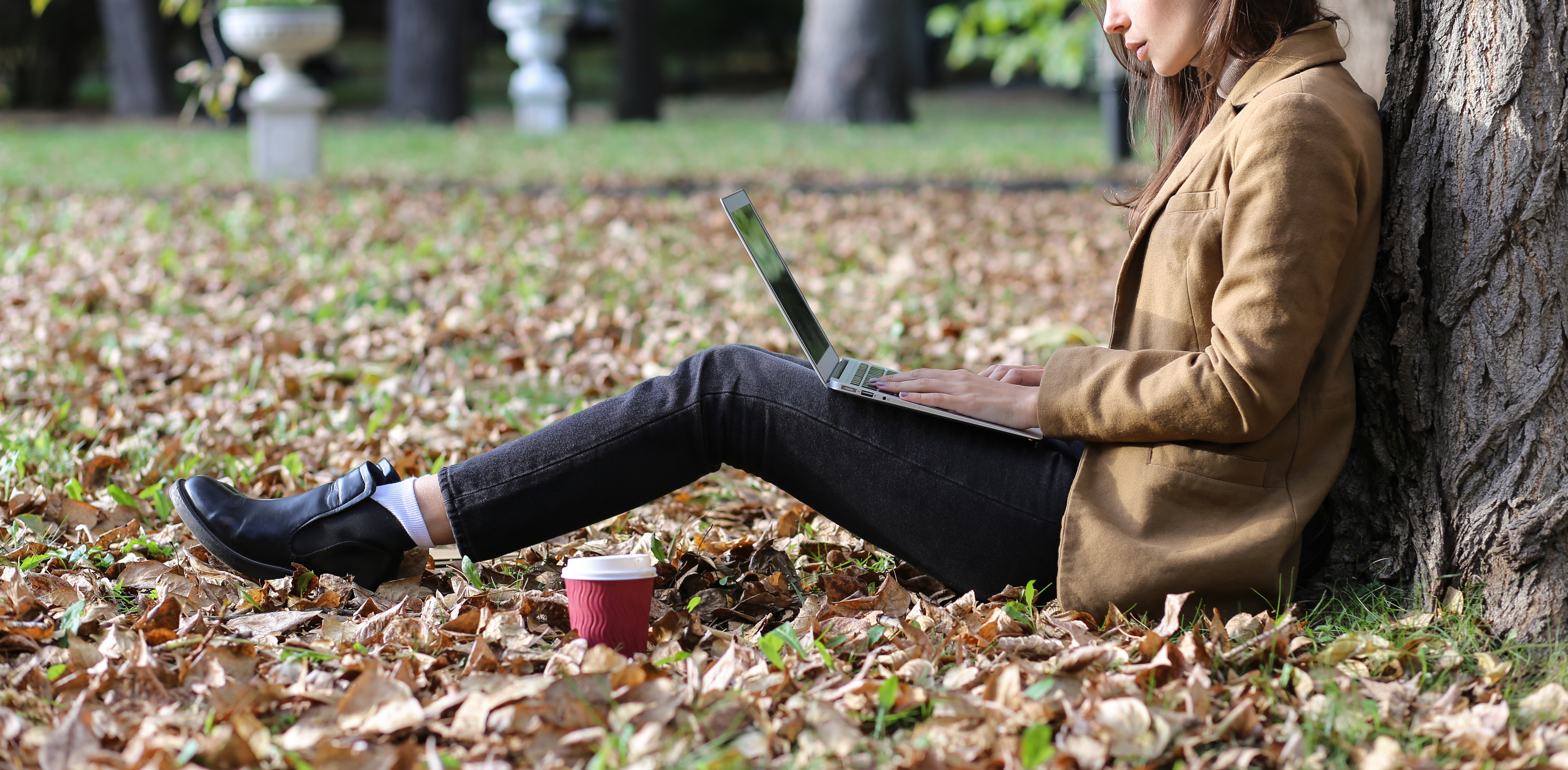 Female professional typing on laptop while sitting outdoors with back against tree