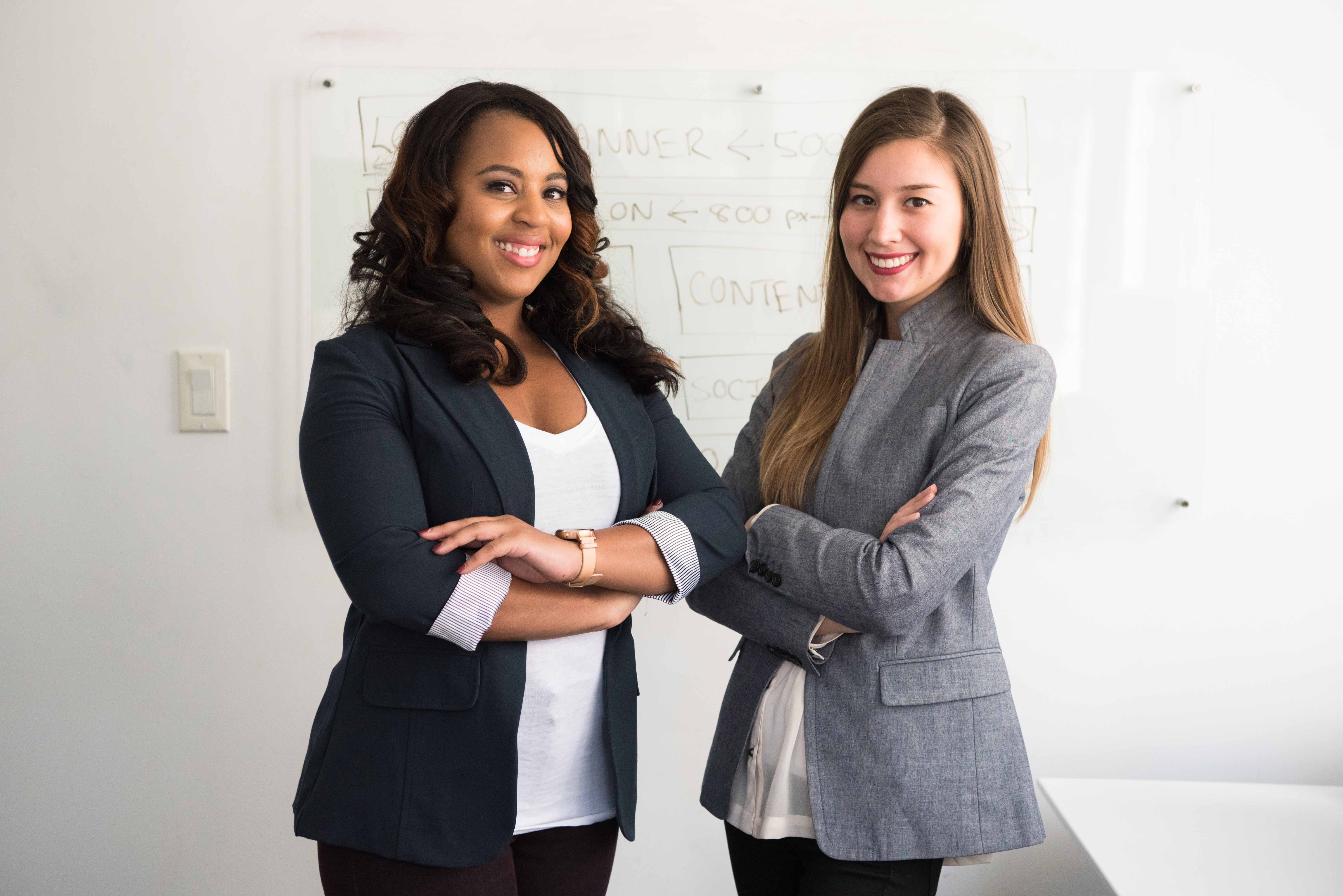Two female professionals in front of a whiteboard.